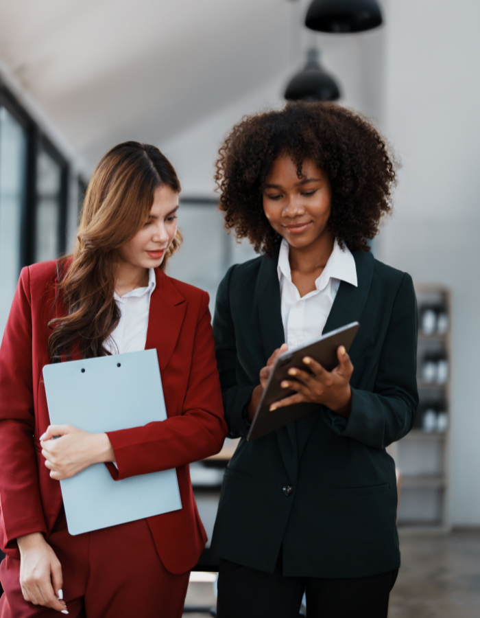 Two professional businesswomen in suits reviewing documents on a tablet together in a modern office