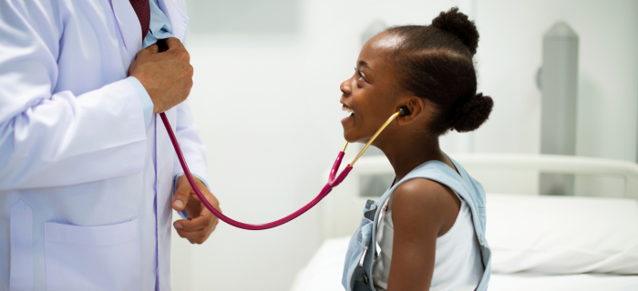 Doctor holding a stethoscope to a young girl's mouth while she smiles playfully