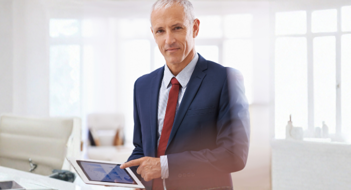 Man in a suit and tie holding a tablet, standing in a bright modern office