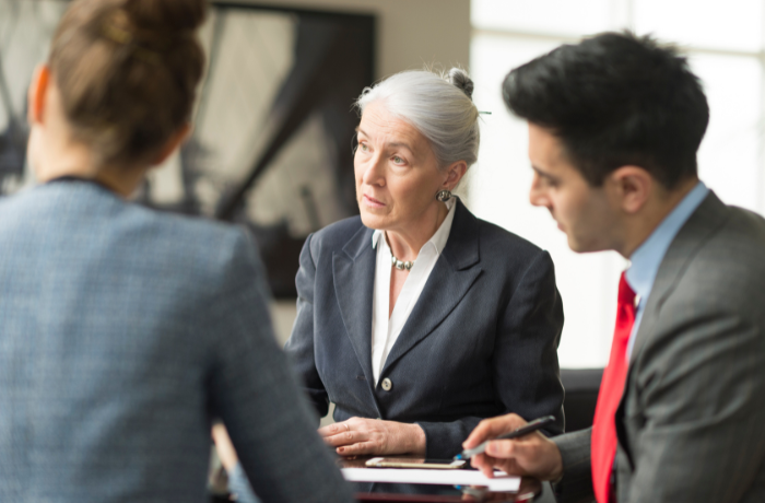 Three professionals in a discussion, with an older woman speaking to two colleagues at a table