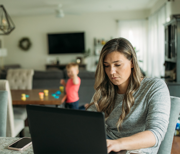 Woman working on a laptop while caring for her children and planning her financial future.