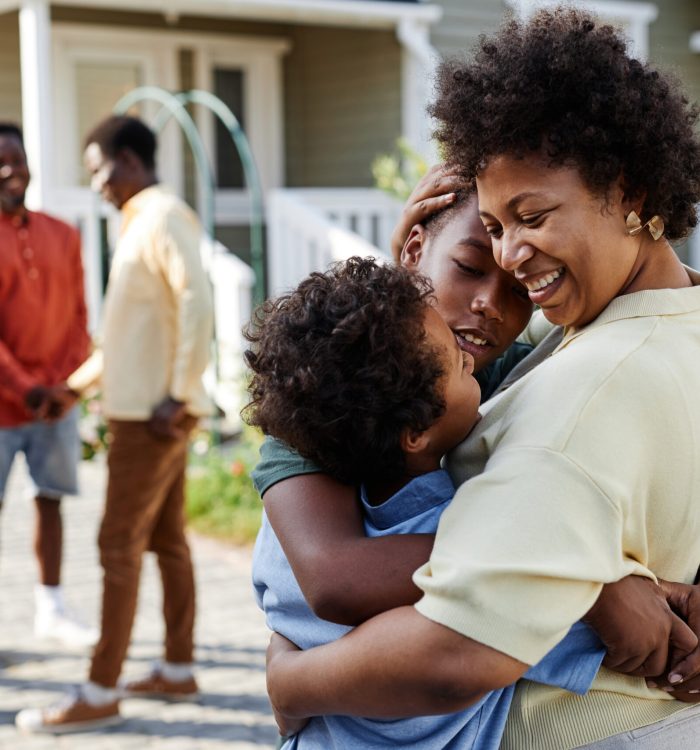 Portrait of smiling black woman embracing two sons at family gathering outdoors, copy space