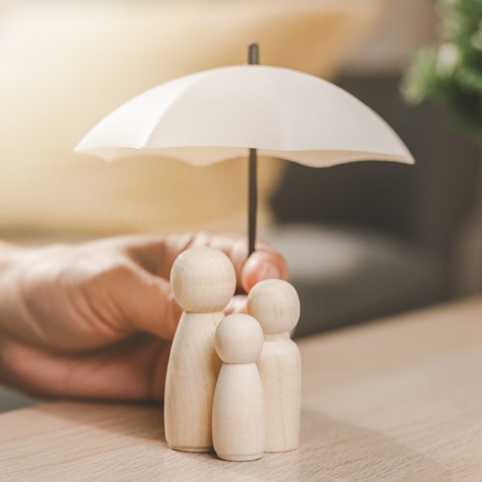 Family insurance plan protect. Help medicine protection. Father mother children insurance. A person holding a white umbrella over a family of three. The umbrella is white and has a black handle.