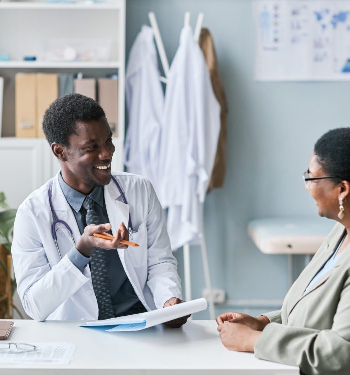 Portrait of smiling black doctor talking to woman during consultation in clinic