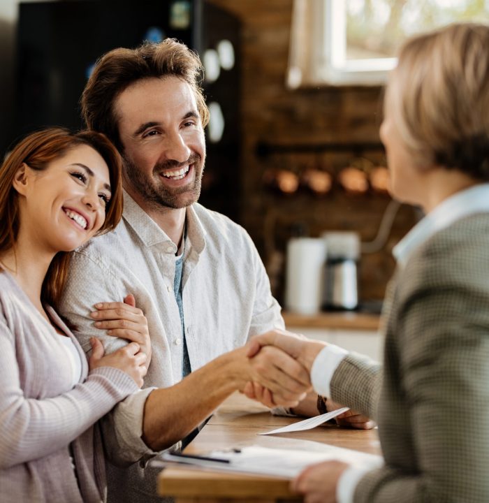 Young happy couple came to an agreement with their insurance agent. Focus is on man shaking hands with the agent.